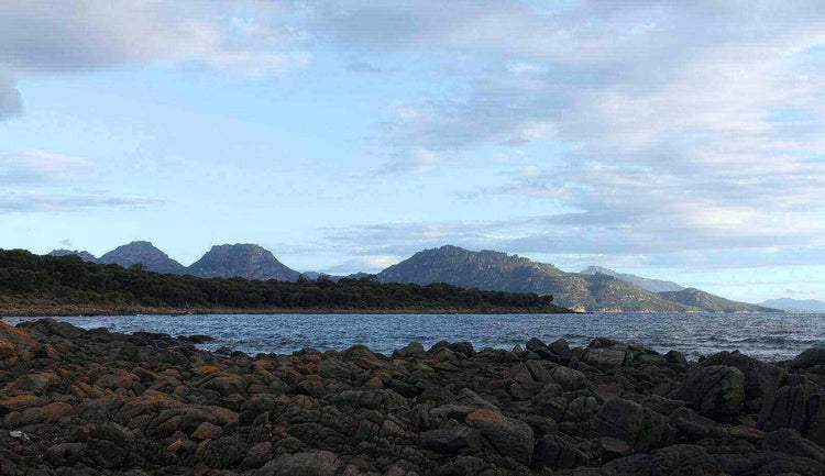 Scenic view of Glass House Mountains in Australia's mountaineering adventure destination, featuring rocky shoreline and lush greenery