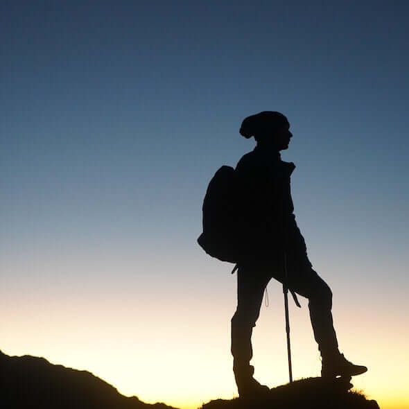 Silhouette of a hiker with a backpack walking stick against a dawn sky in Australia illustrating outdoor adventure.