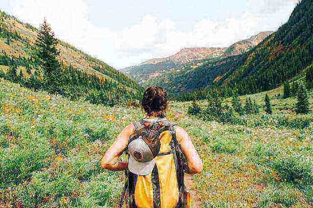 Hiker with a yellow backpack explores a lush, mountainous landscape, embodying the natural connection promoted by Vivobarefoot footwear.