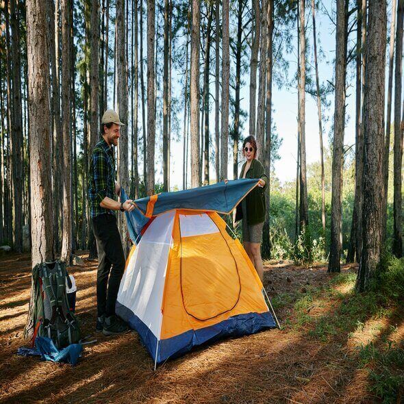 Campers setting up a tent in a forest for a safe outdoor adventure.