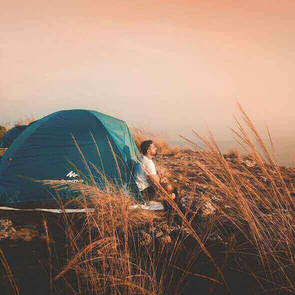 Solo camper relaxing beside tent at sunrise, embracing nature and solitude for mental recharge