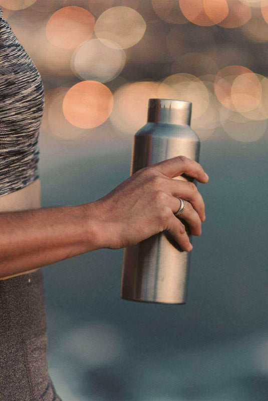 Person holding a stainless steel water bottle outdoors with a blurred background