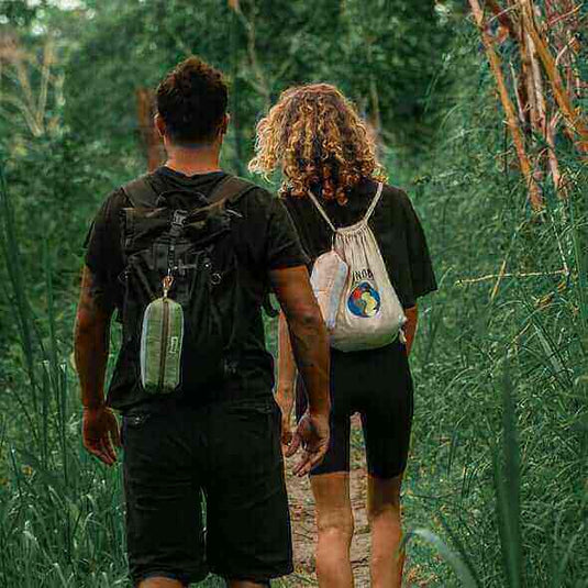 Two hikers wearing black outfits and backpacks walking on a lush green forest trail.