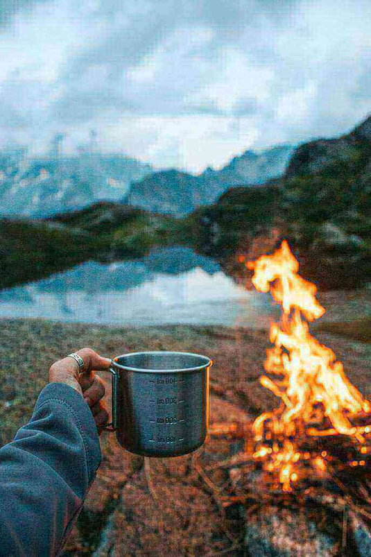 Enjoying a hot drink by a campfire in the wilderness, essential for staying hydrated while camping.