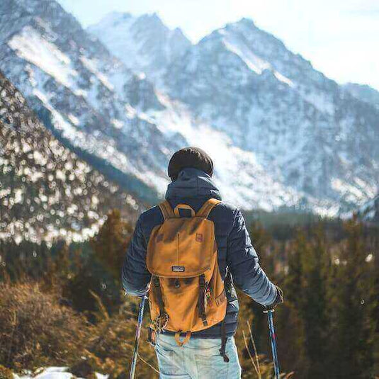 Hiker with disabilities equipped with trekking poles and backpack, exploring snowy mountain trail.