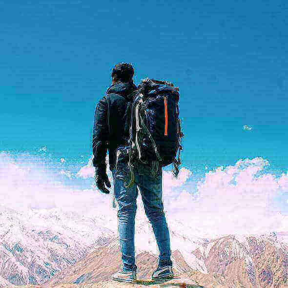 Hiker with a dry bag stands on mountain overlooking snowy peaks and blue sky.