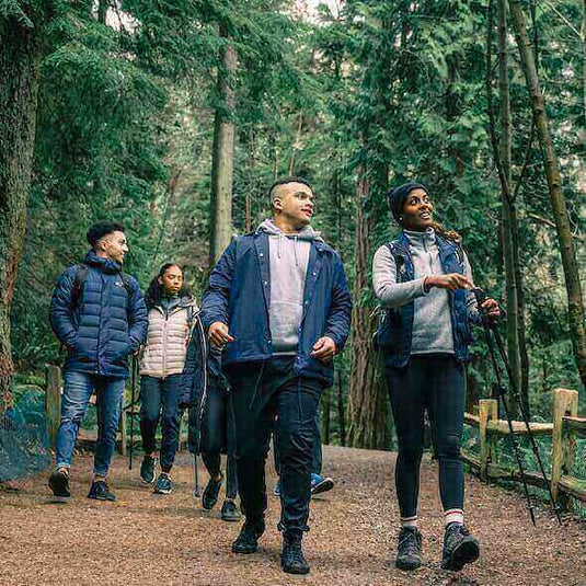 Group of hikers wearing essential clothing and gear, walking on a forest trail.