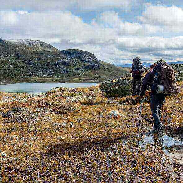 Two trekkers with essential gear hiking in a scenic mountainous landscape with a lake in the background