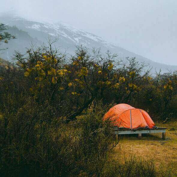 Orange tent set up in a minimalist camping spot surrounded by nature, mountains in the background.