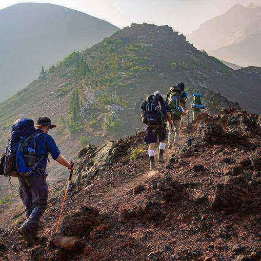 Hikers carrying backpacks hiking uphill on a rocky trail to avoid dehydration during outdoor activity - Adventureco Blog