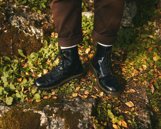 Black Doc Martens boots on rocky terrain surrounded by green foliage and autumn leaves.