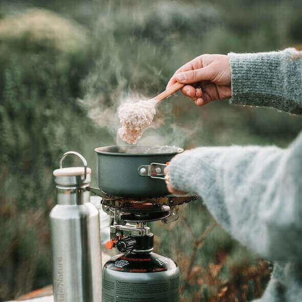 Cooking sustainable meal on eco-friendly camping stove with reusable water bottle in the background