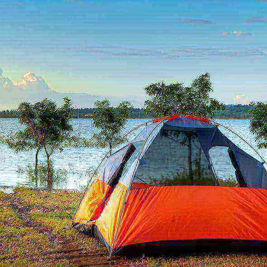 Red and gray camping tent set up near a lake with trees in the background, ideal for outdoor adventures and nature trips.