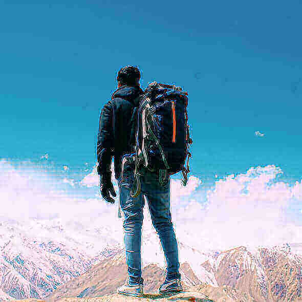 Backpacker standing on a mountain peak, showcasing light packing essentials for long hikes with scenic snowy mountains in the background.