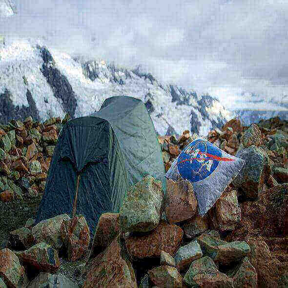 Camping pillow next to a tent on rocky terrain with snowy mountains in the background