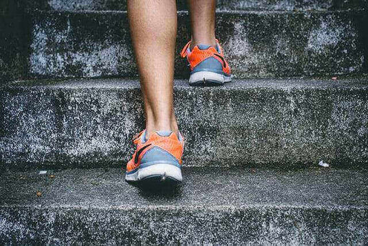 Person wearing sporty orange and grey shoes walking up concrete stairs, illustrating modern athletic shoe styles. - Adventureco Blog