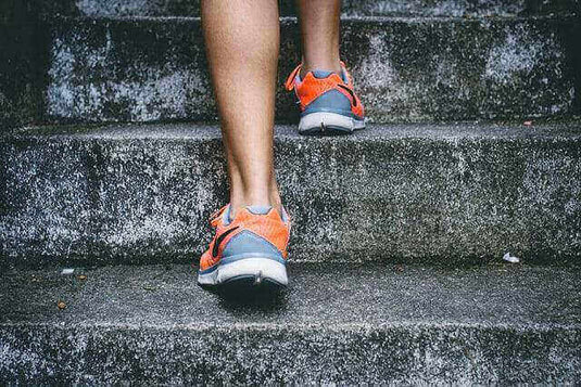 Person wearing sporty orange and grey shoes walking up concrete stairs, illustrating modern athletic shoe styles.