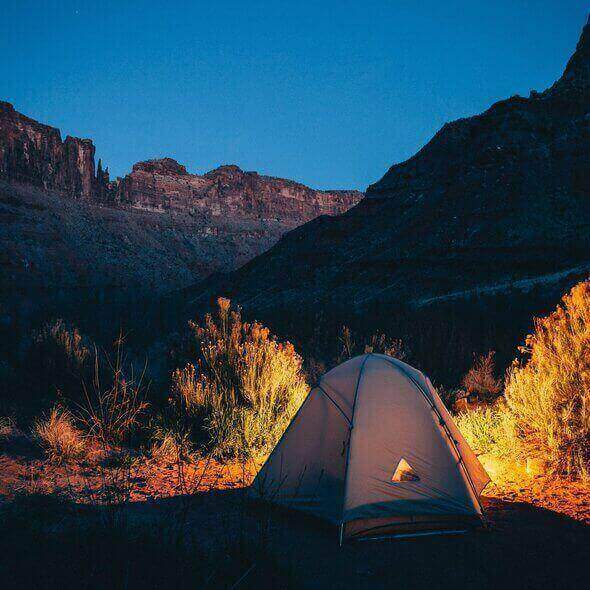 Solo camping trip at night with a glowing tent in a serene desert landscape under a clear blue sky.