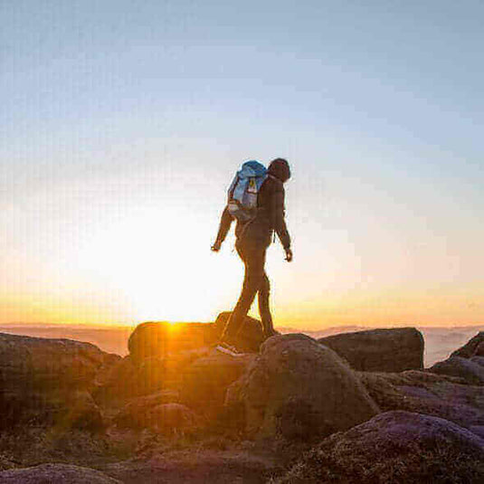 Trekker with backpack walking on rocky terrain at sunrise, highlighting the adventure and beauty of trekking for beginners.