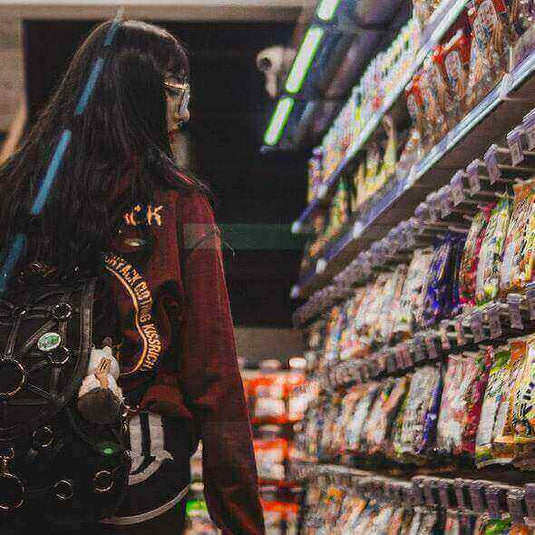 Woman shopping for snacks in a grocery store aisle wearing a backpack.