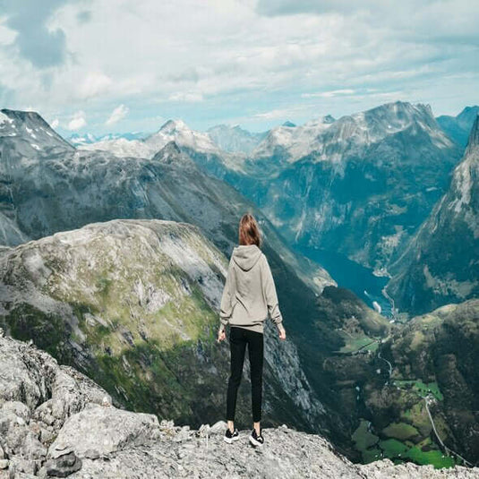 Person standing on a mountain peak, admiring a breathtaking view of valleys and surrounding hills.