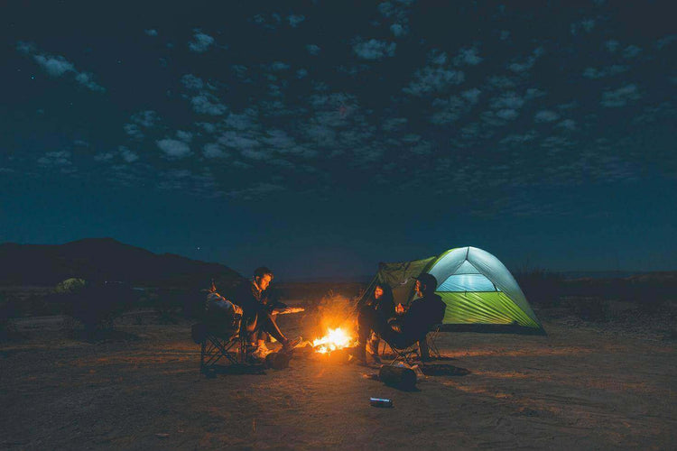 Campers sitting around a campfire near a glowing tent under a starry sky, enjoying a peaceful night in nature.