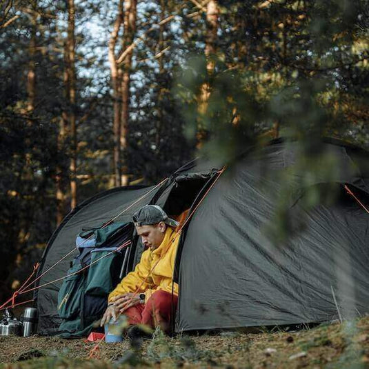 Camper in a forest setting using eco-friendly camping gear outside a tent