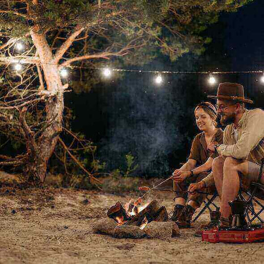 Couple enjoying a zero waste camping experience with campfire under string lights in the woods