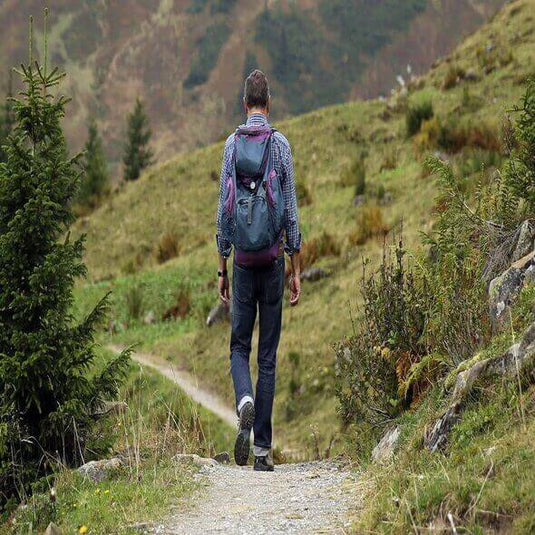 A hiker with a backpack walking on a nature trail surrounded by greenery and mountains in Australia. - Adventureco Blog