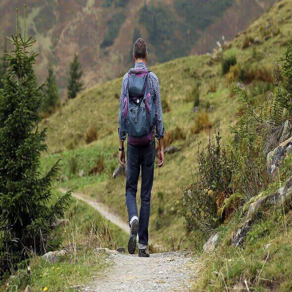 A hiker with a backpack walking on a nature trail surrounded by greenery and mountains in Australia.