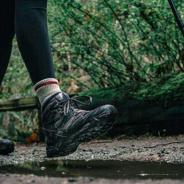 Close-up of hiker wearing sturdy hiking boots on a muddy trail in the forest.