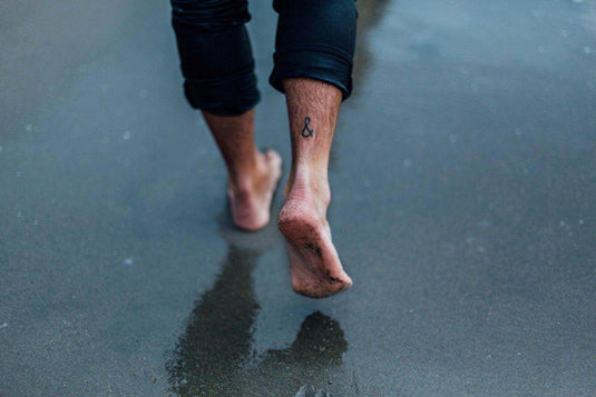Barefoot person walking on wet sandy surface illustrating benefits of wearing barefoot shoes - Adventureco Blog