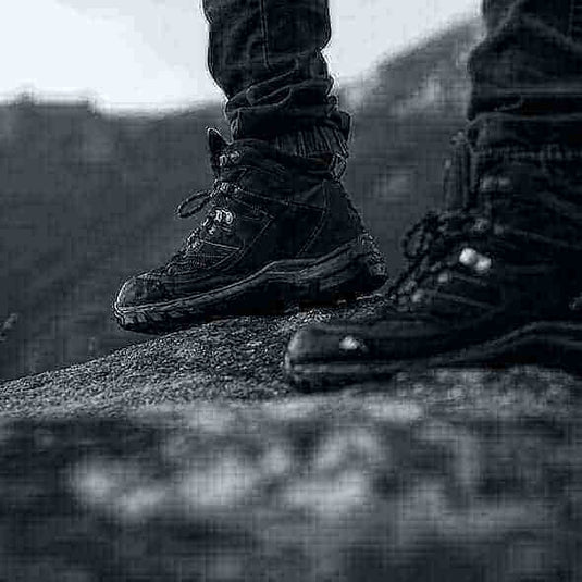 Close-up of a hiker wearing sturdy black hiking boots standing on rocky terrain.