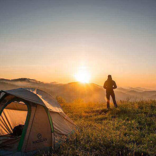 Person standing near a tent, admiring a sunrise in the Australian wilderness, embodying eco-friendly camping adventures. - Adventureco Blog