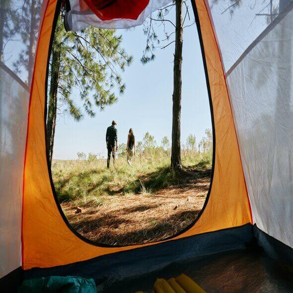 View from inside a camping tent looking out at two people walking in an Australian campground surrounded by trees and grass.