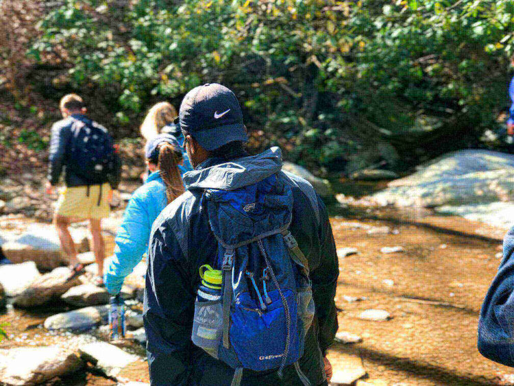 Hikers dressed in layered clothing on a spring hike, crossing a shallow stream in a forested area