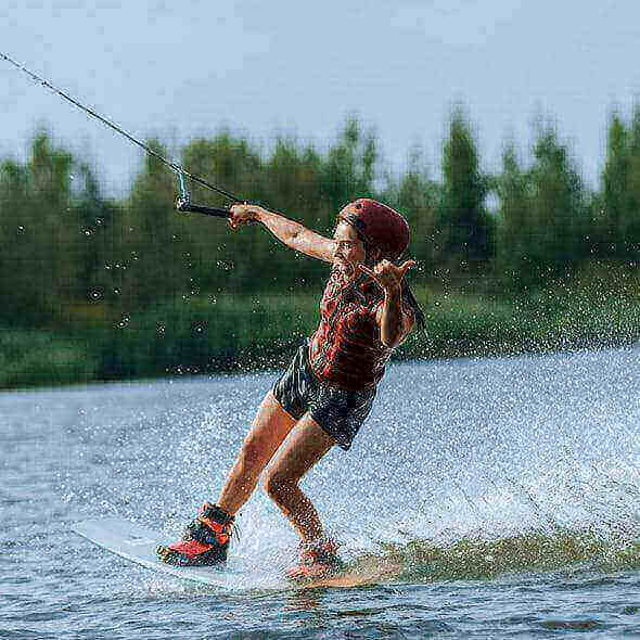 Person wakeboarding on a lake wearing a red helmet and life vest, following outdoor adventure safety tips.