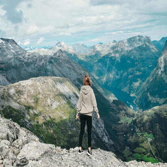 Person standing on a mountain peak, admiring a breathtaking view of valleys and surrounding hills. - Adventureco Blog