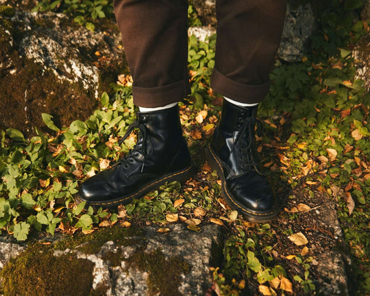 Black Doc Martens boots on rocky terrain surrounded by green foliage and autumn leaves.