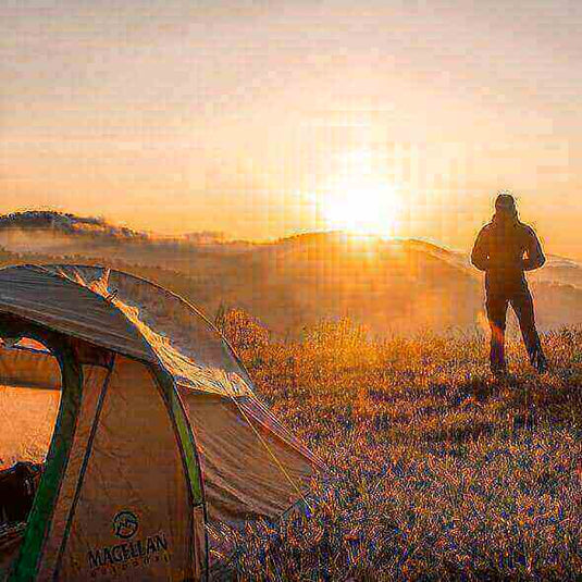 Sunrise view from a camping tent with a hiker standing nearby in nature - Adventureco Blog