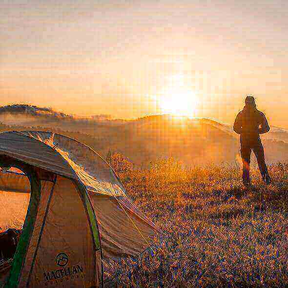 Sunrise view from a camping tent with a hiker standing nearby in nature