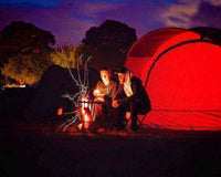 Campers enjoy a sustainable camping trip by a fire in front of a red tent under the night sky.