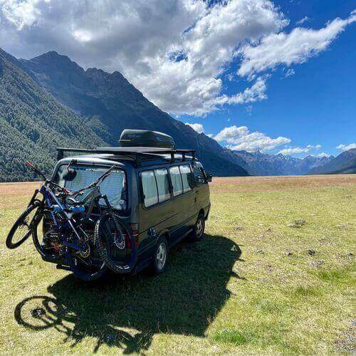 Campervan with bikes attached, parked in a scenic mountain landscape under a bright blue sky, perfect for an adventure.