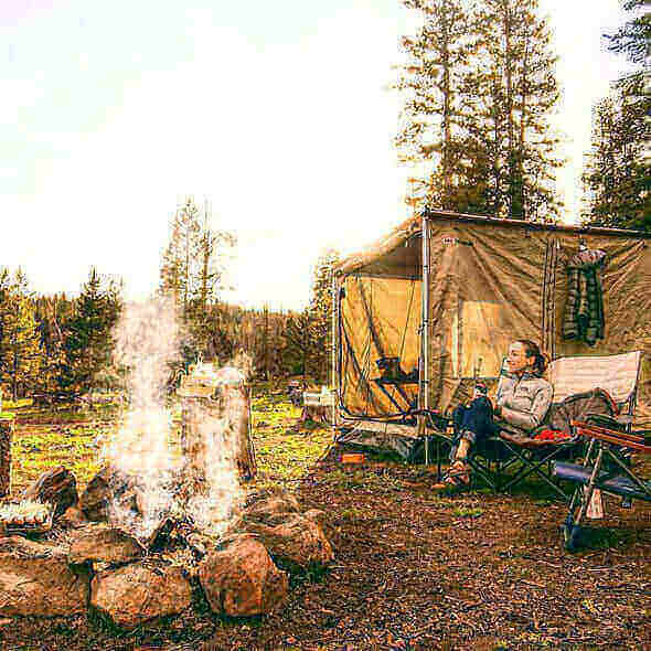 Camper relaxing by a tent and campfire in a forest, enjoying the great outdoors with essential camping gear.