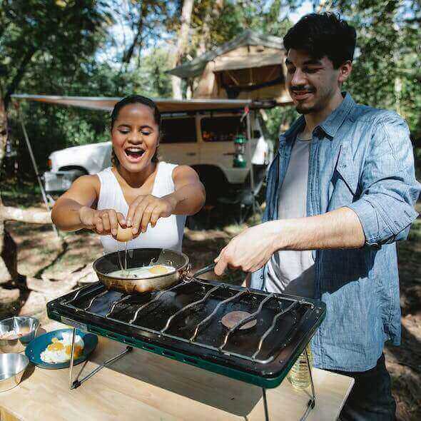 Campers cooking breakfast together in a forest, promoting sustainable camp cooking with a portable stove.