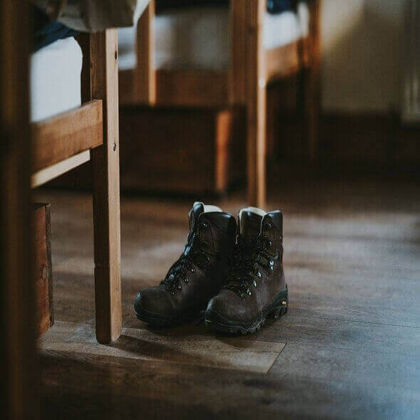 Sustainable hiking boots on wooden floor under bed in cozy cabin