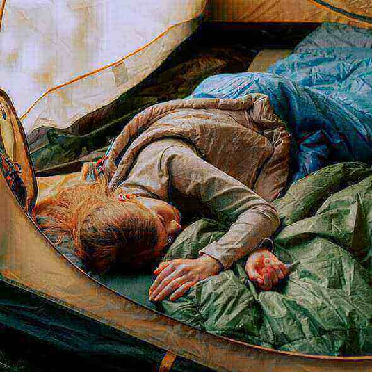 Woman sleeping comfortably in a tent with a cozy sleeping bag while camping in the wilderness. - Adventureco Blog