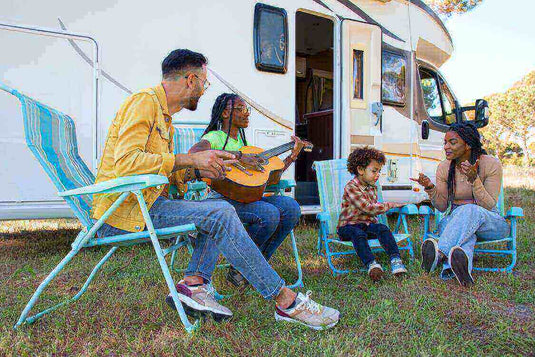 Family enjoying a caravan adventure, playing guitar and relaxing beside their camper on a grassy field.