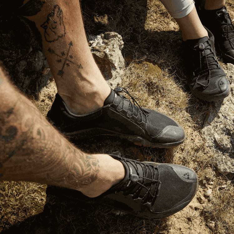 Two trail runners wearing black trail running shoes resting on rocky terrain