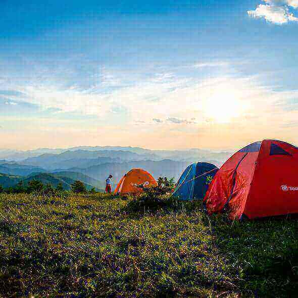 Colorful tents set up on a grassy hilltop with a stunning mountain view at sunrise, perfect for beginner campers exploring the outdoors.